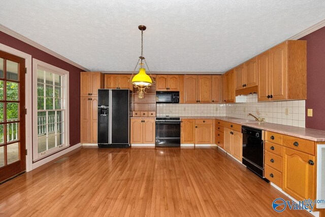 kitchen with light wood finished floors, black appliances, a sink, light countertops, and decorative backsplash