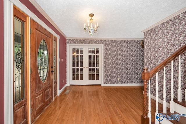 entryway with crown molding, french doors, light wood-style floors, an inviting chandelier, and a textured ceiling