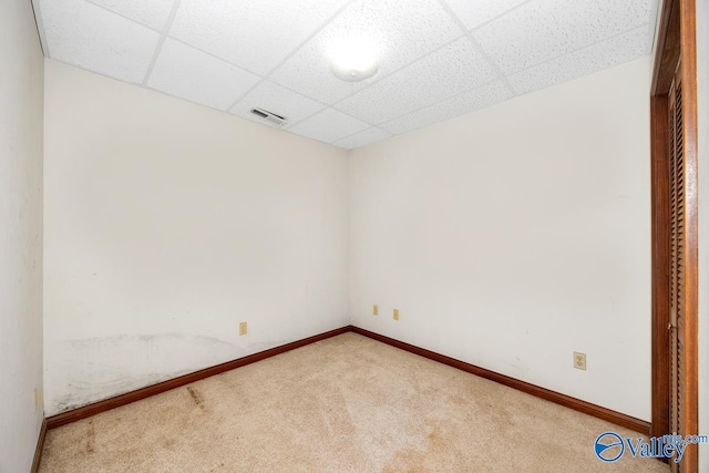 carpeted spare room with visible vents, a paneled ceiling, and baseboards