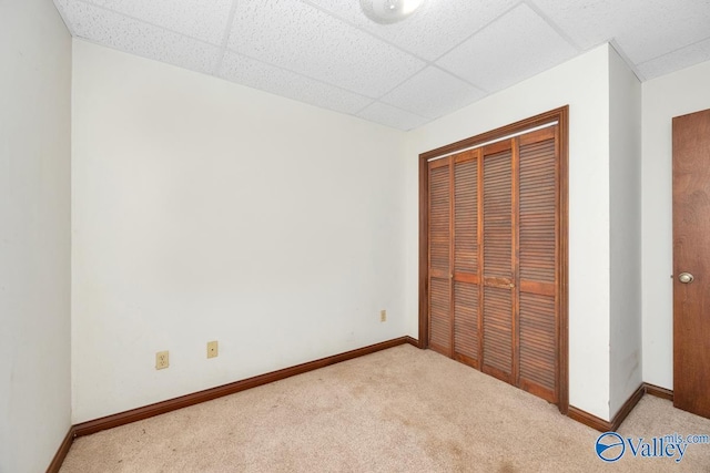 unfurnished bedroom featuring a closet, baseboards, a paneled ceiling, and carpet