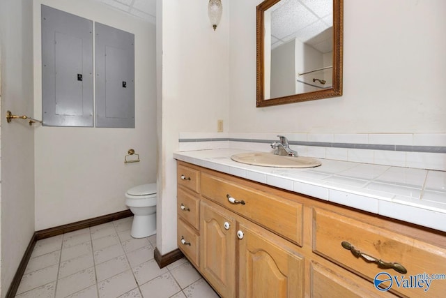 bathroom featuring electric panel, toilet, vanity, and baseboards