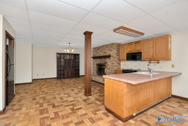 kitchen with a brick fireplace, tile counters, a peninsula, black appliances, and a sink