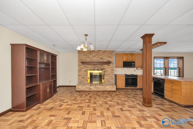 unfurnished living room featuring a drop ceiling, a fireplace, baseboards, and decorative columns
