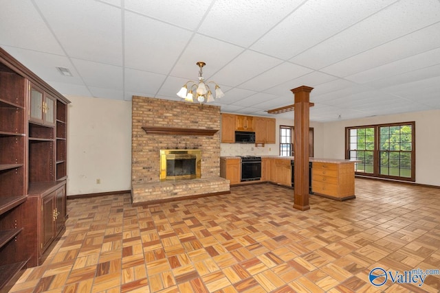 unfurnished living room with visible vents, a drop ceiling, a fireplace, decorative columns, and baseboards