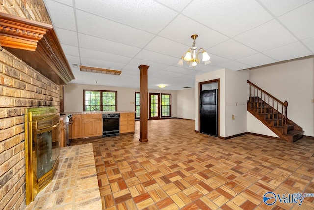 unfurnished living room with stairs, a brick fireplace, a paneled ceiling, and baseboards
