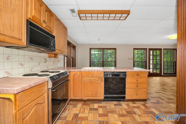 kitchen featuring backsplash, black microwave, tile counters, a peninsula, and electric stove