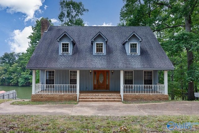 cape cod house with roof with shingles, a porch, a chimney, a water view, and board and batten siding
