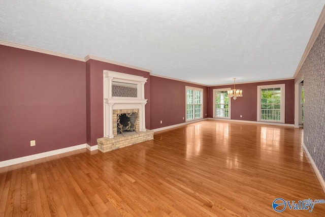 unfurnished living room with a brick fireplace, a chandelier, ornamental molding, and light wood finished floors