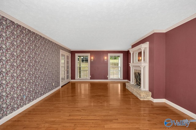 unfurnished living room featuring wallpapered walls, baseboards, and wood finished floors
