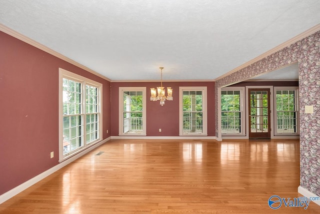 unfurnished living room featuring plenty of natural light, a notable chandelier, light wood-style flooring, and crown molding