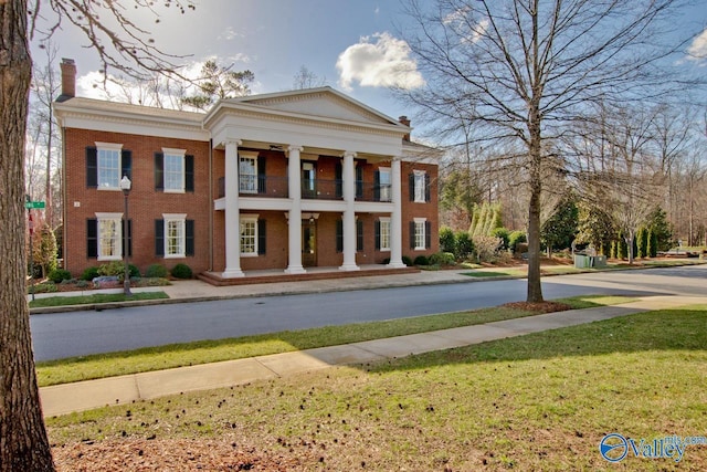 view of front of home with a porch, brick siding, a balcony, a front lawn, and a chimney