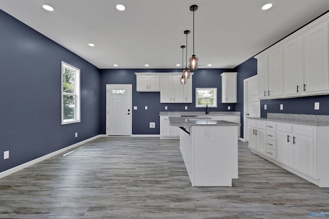 kitchen featuring white cabinets, light stone counters, light hardwood / wood-style floors, decorative light fixtures, and a center island