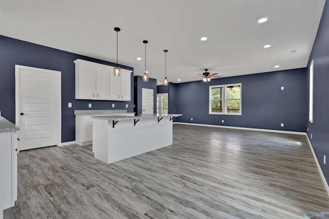 kitchen featuring white cabinetry, light wood-type flooring, a center island, a breakfast bar area, and light stone countertops