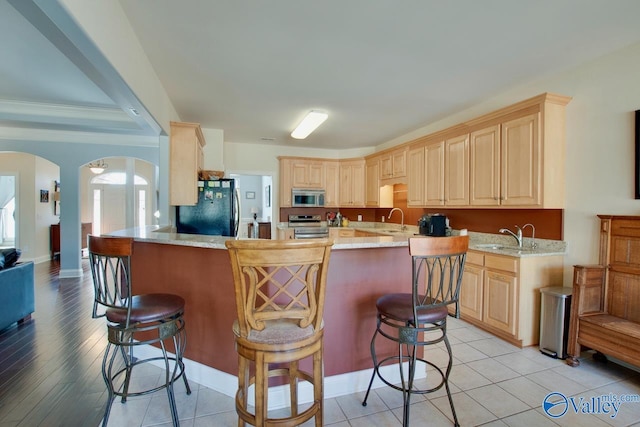 kitchen featuring light brown cabinets, a sink, appliances with stainless steel finishes, and arched walkways