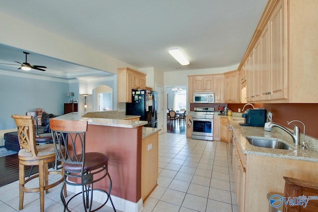 kitchen featuring a breakfast bar, light brown cabinets, stainless steel appliances, and a sink