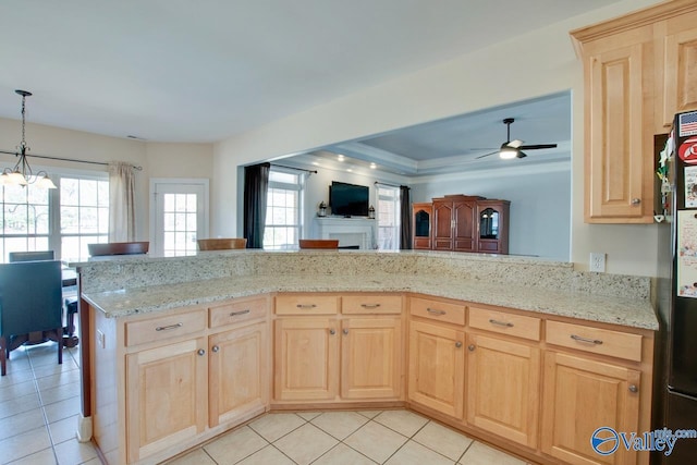 kitchen featuring light stone countertops, ceiling fan with notable chandelier, light brown cabinets, and freestanding refrigerator