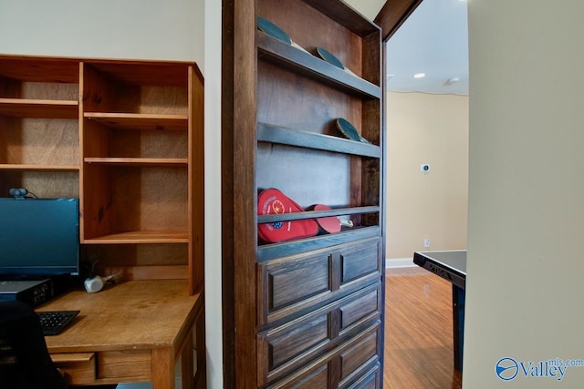 office space featuring wood finished floors, built in desk, and baseboards