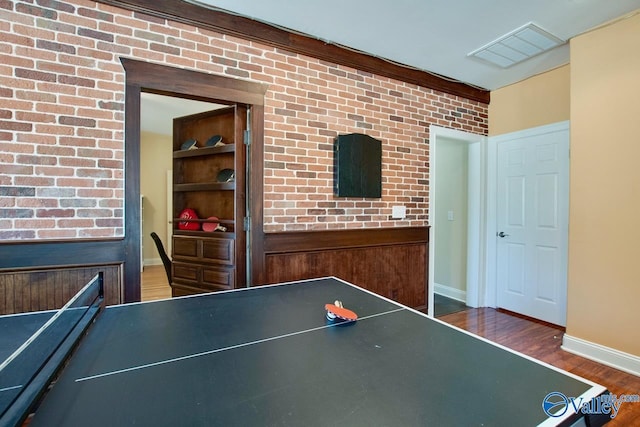 rec room with visible vents, baseboards, wood finished floors, and brick wall