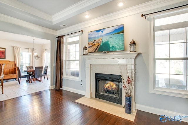 living area featuring wood finished floors, baseboards, a tiled fireplace, crown molding, and a raised ceiling