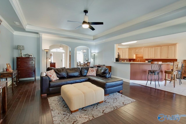 living area featuring a raised ceiling, arched walkways, and dark wood-type flooring