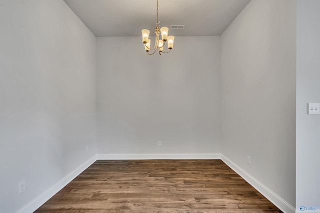 spare room with a chandelier, dark wood-style flooring, visible vents, and baseboards