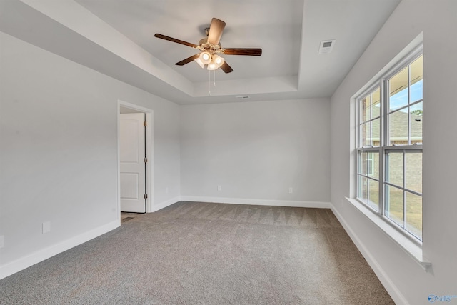 carpeted spare room with a tray ceiling, visible vents, ceiling fan, and baseboards