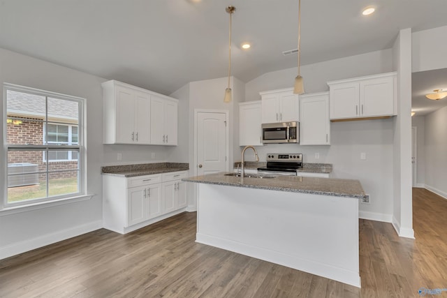 kitchen with appliances with stainless steel finishes, white cabinets, a sink, dark stone countertops, and an island with sink