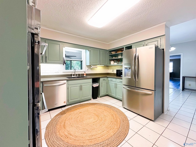 kitchen with light tile patterned floors, a sink, stainless steel appliances, and green cabinetry