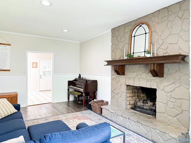 living area with ornamental molding, a textured ceiling, a wainscoted wall, a stone fireplace, and wood finished floors