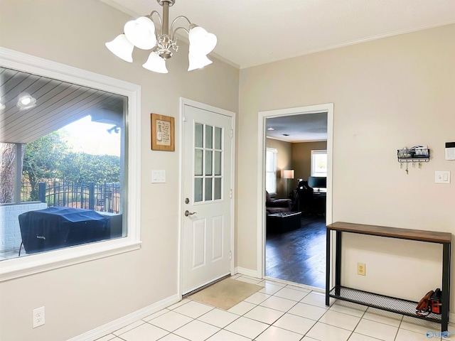 foyer featuring light tile patterned flooring, ornamental molding, baseboards, and a chandelier