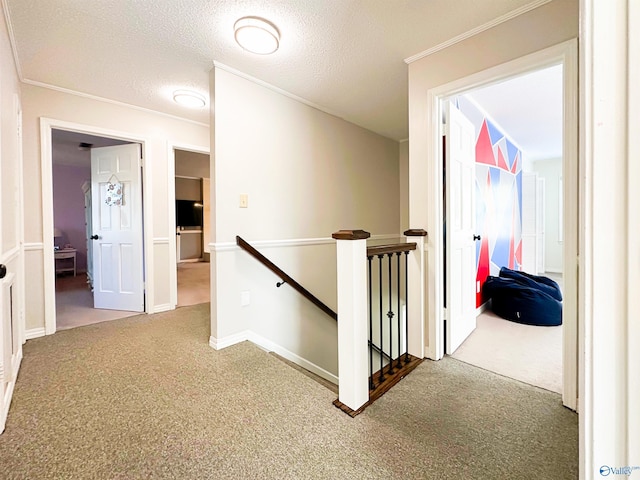 corridor with a textured ceiling, carpet floors, an upstairs landing, and ornamental molding