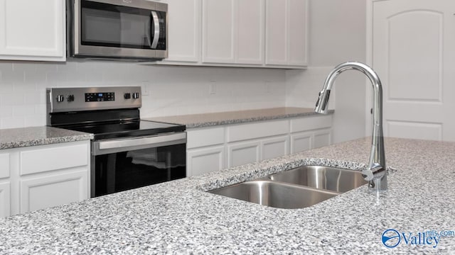 kitchen with appliances with stainless steel finishes, light stone counters, white cabinetry, and sink