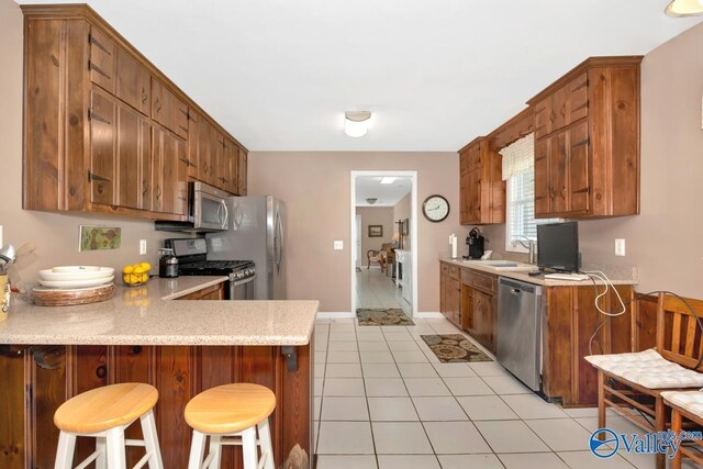 kitchen featuring light tile patterned flooring, kitchen peninsula, appliances with stainless steel finishes, a kitchen breakfast bar, and sink