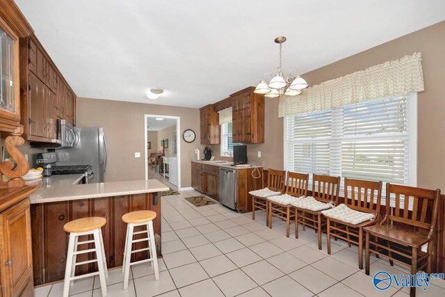 kitchen with a notable chandelier, decorative light fixtures, light tile patterned floors, stainless steel appliances, and kitchen peninsula