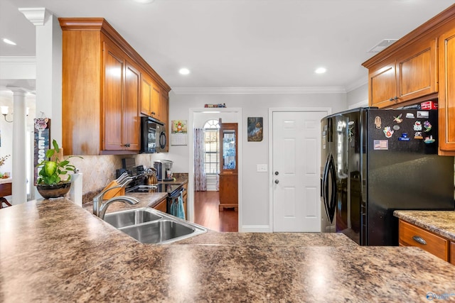 kitchen featuring black appliances, decorative columns, brown cabinetry, and a sink