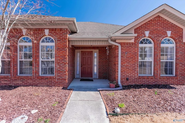 property entrance with a shingled roof and brick siding