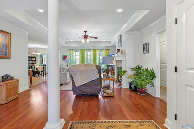 living room featuring ornamental molding, ceiling fan with notable chandelier, decorative columns, and wood finished floors