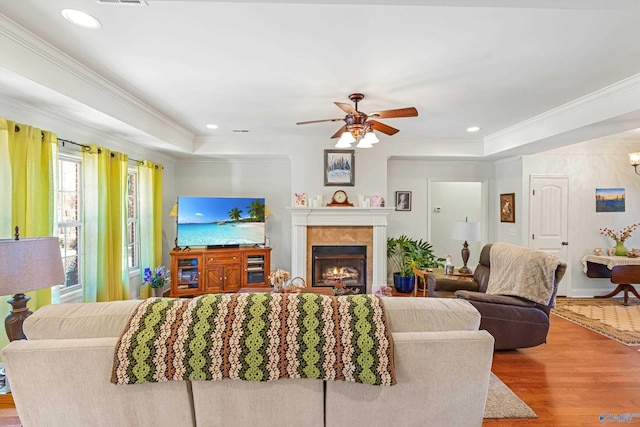 living area with recessed lighting, crown molding, a lit fireplace, and wood finished floors