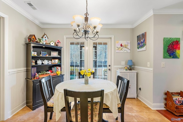 dining room featuring visible vents, a wainscoted wall, ornamental molding, an inviting chandelier, and french doors