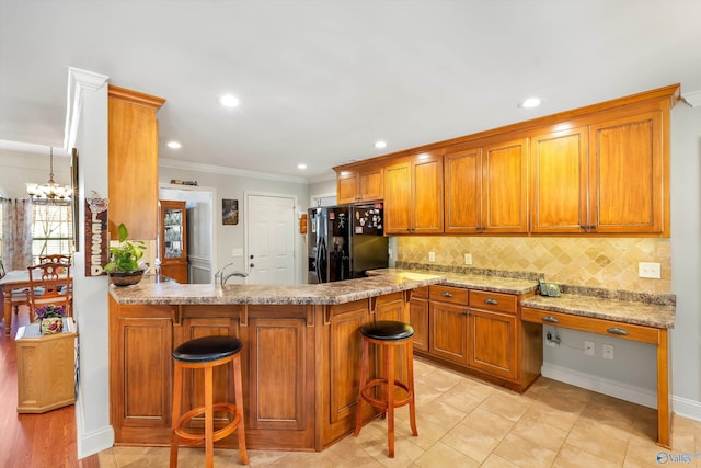 kitchen with black refrigerator with ice dispenser, brown cabinetry, a kitchen bar, and backsplash