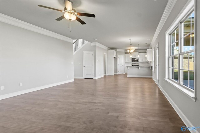 unfurnished living room featuring ornamental molding, dark hardwood / wood-style floors, and ceiling fan with notable chandelier