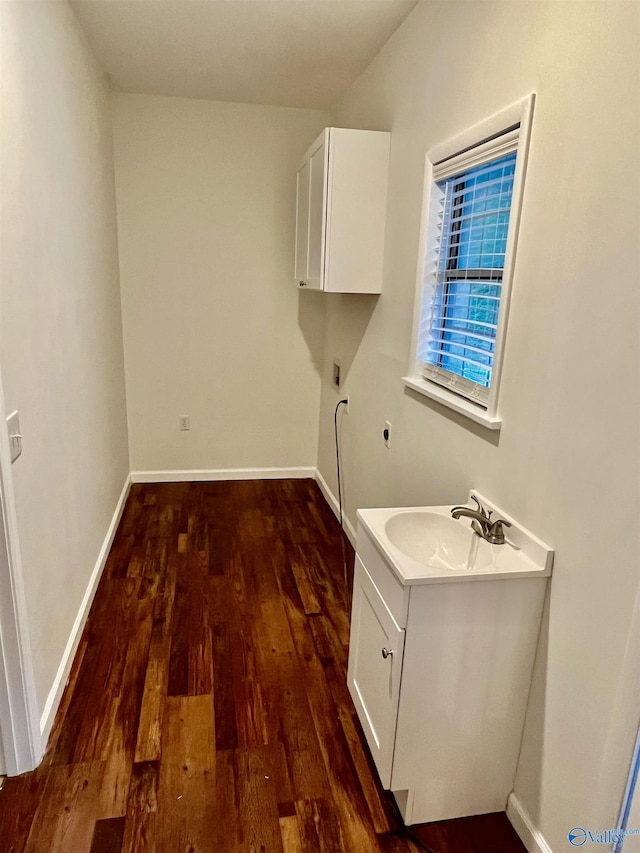 clothes washing area with a sink, hookup for an electric dryer, baseboards, cabinet space, and dark wood-type flooring