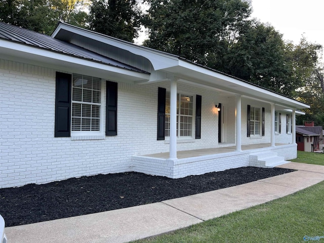 exterior space with metal roof, covered porch, and brick siding
