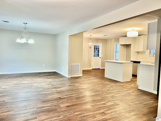 unfurnished living room featuring wood finished floors, baseboards, a chandelier, and visible vents
