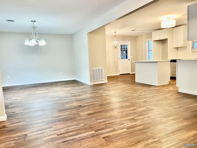 unfurnished living room with baseboards, light wood-style flooring, visible vents, and an inviting chandelier