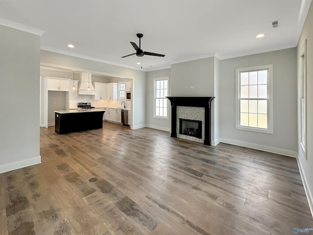 unfurnished living room with sink, a tile fireplace, ceiling fan, wood-type flooring, and ornamental molding