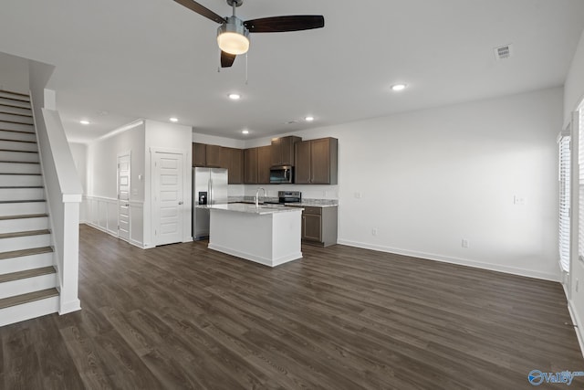 kitchen with light stone counters, dark hardwood / wood-style floors, stainless steel appliances, a kitchen island with sink, and ceiling fan