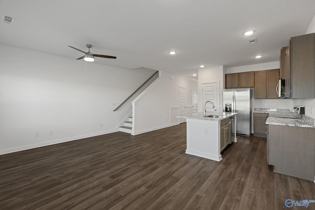 kitchen with sink, stainless steel appliances, light stone countertops, and a center island with sink