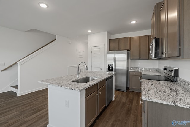 kitchen featuring stainless steel appliances, sink, light stone counters, a kitchen island with sink, and dark wood-type flooring