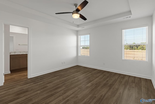 unfurnished room with ceiling fan, a tray ceiling, and dark hardwood / wood-style floors